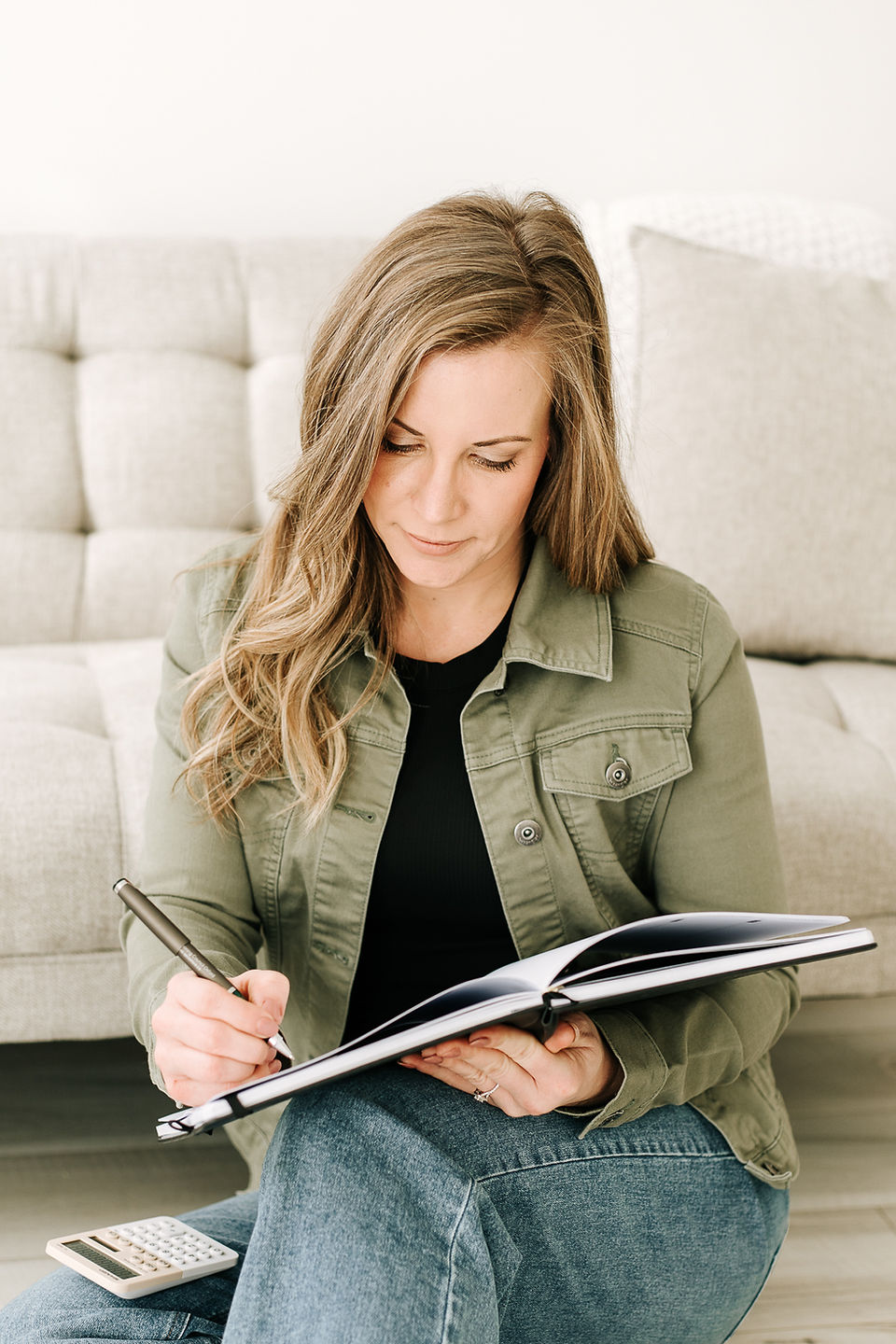 Woman accountant in an olive green jacket sitting on the floor with an open binder, creating a relaxed and casual branding portrait.