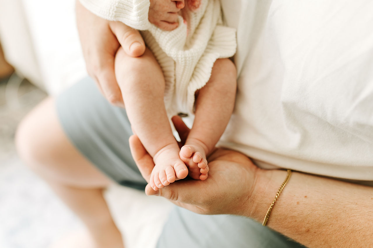 Newborn photography in Guelph, Ontario capturing baby's tiny feet and legs held gently by a parent during an in-home session