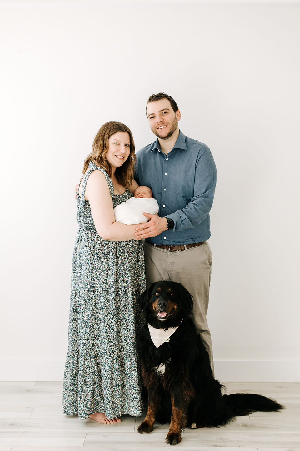 Studio newborn session in Guelph, Ontario featuring parents holding their newborn baby with family dog in a bright, minimalist studio portrait