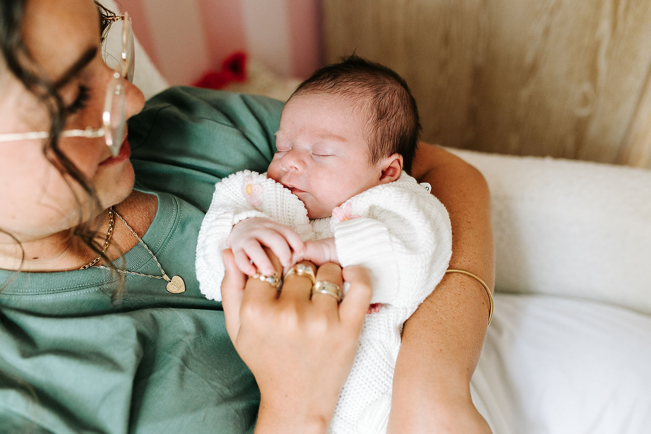In-home newborn session in Guelph, Ontario featuring mom cuddling her sleeping newborn in a nursery with hand-painted striped walls