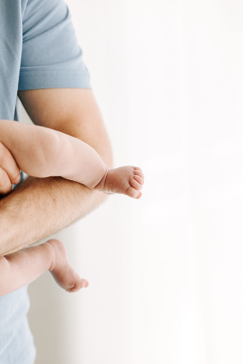 Newborn baby in father's arms during a studio newborn session in Guelph, Ontario captured with soft natural light and minimalist styling