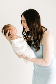 Newborn session in Guelph, Ontario featuring mom in light blue dress holding sleeping newborn baby in a timeless studio portrait