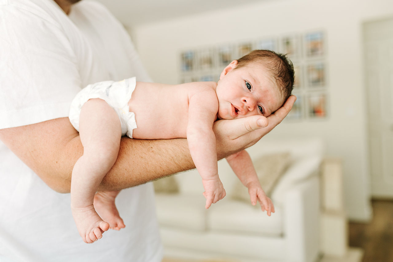 In-home newborn session in Guelph, Ontario featuring dad gently holding their newborn in a football hold in a bright living room