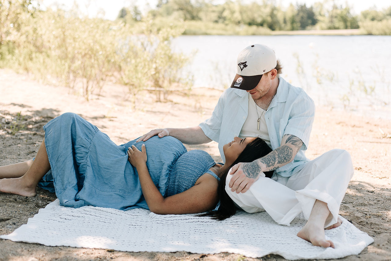 Maternity session in Guelph, Ontario featuring mom and dad-to-be sharing a loving moment on a sandy beach beside the lake