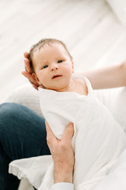 Newborn session in Guelph, Ontario capturing parents holding newborn baby wrapped in white swaddle in a clean minimalist studio setup