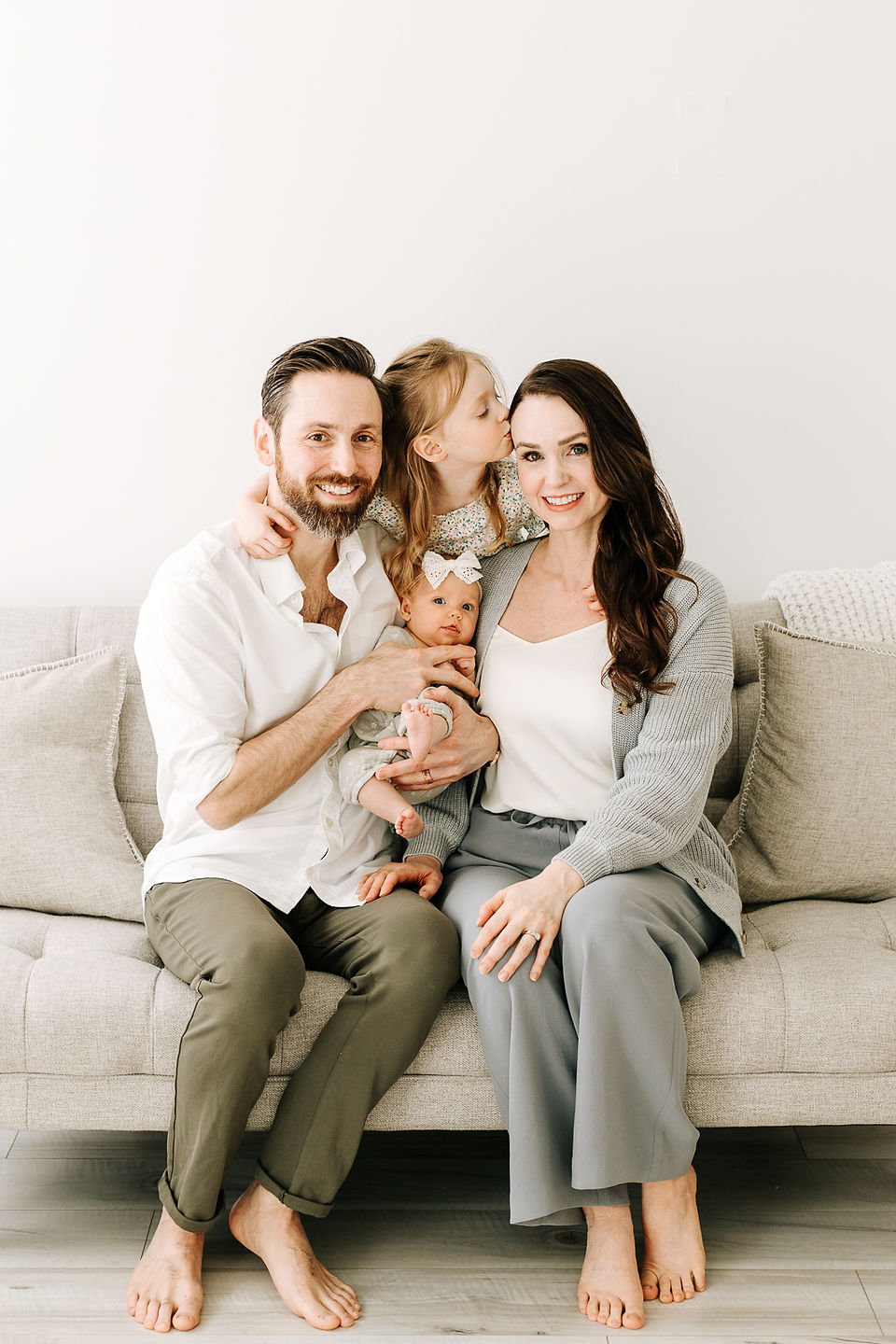 Family of four during a newborn session in Guelph, Ontario, sitting closely together with newborn baby and older sister in a soft studio setting