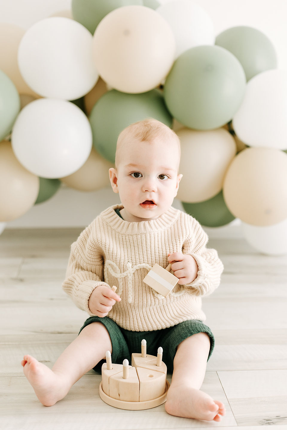 Milestone session in Guelph, Ontario featuring baby boy in a cream knit sweater playing with a wooden toy on a light wood floor