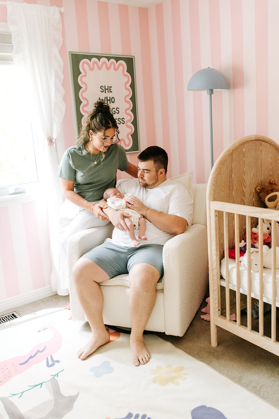 In-home newborn session in Guelph, Ontario featuring parents cuddling their newborn baby in a nursery with hand-painted pink and white striped walls