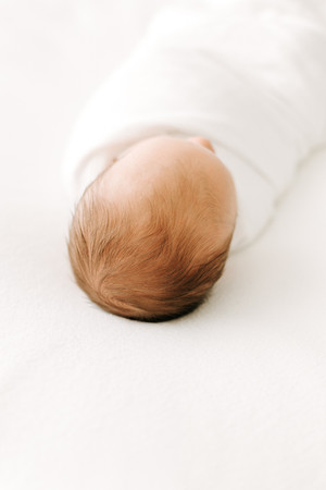 Sleeping newborn baby wrapped in a white swaddle during a newborn session in Guelph, Ontario in a soft, minimal studio portrait
