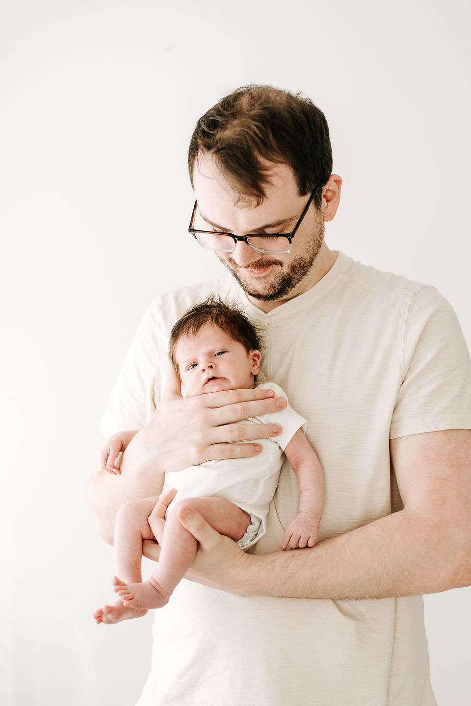 Dad holding newborn baby during a newborn session in Guelph, Ontario in a soft and natural studio portrait