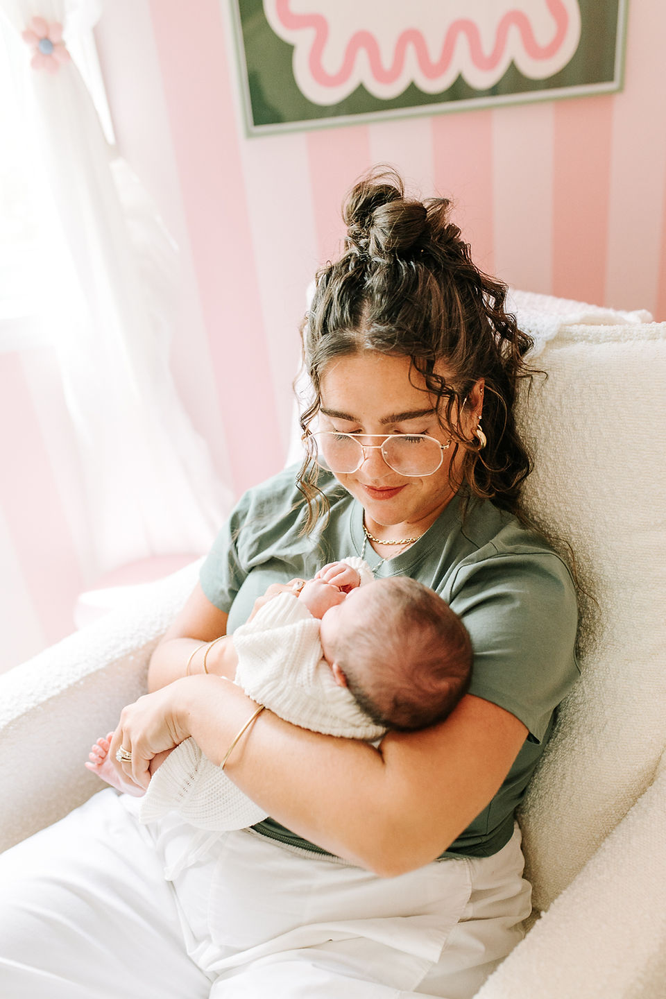 Newborn photography in Guelph, Ontario capturing mom cradling her sleeping baby against a nursery wall hand-painted with stripes by dad