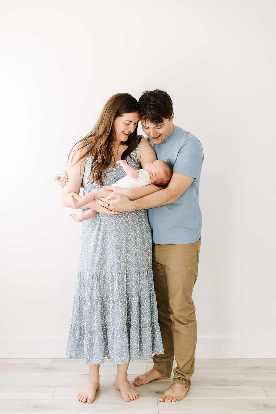 Family of three posing during a studio newborn session in Guelph, Ontario with newborn baby held in mom's arms against a white studio background