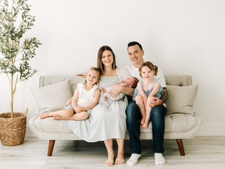 Family of five posing on a beige couch during an in-home newborn photography session in Guelph, Ontario, with a decorative olive tree beside them.