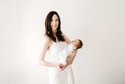 Newborn session in Guelph, Ontario featuring mother holding swaddled newborn baby in a bright, minimal studio portrait