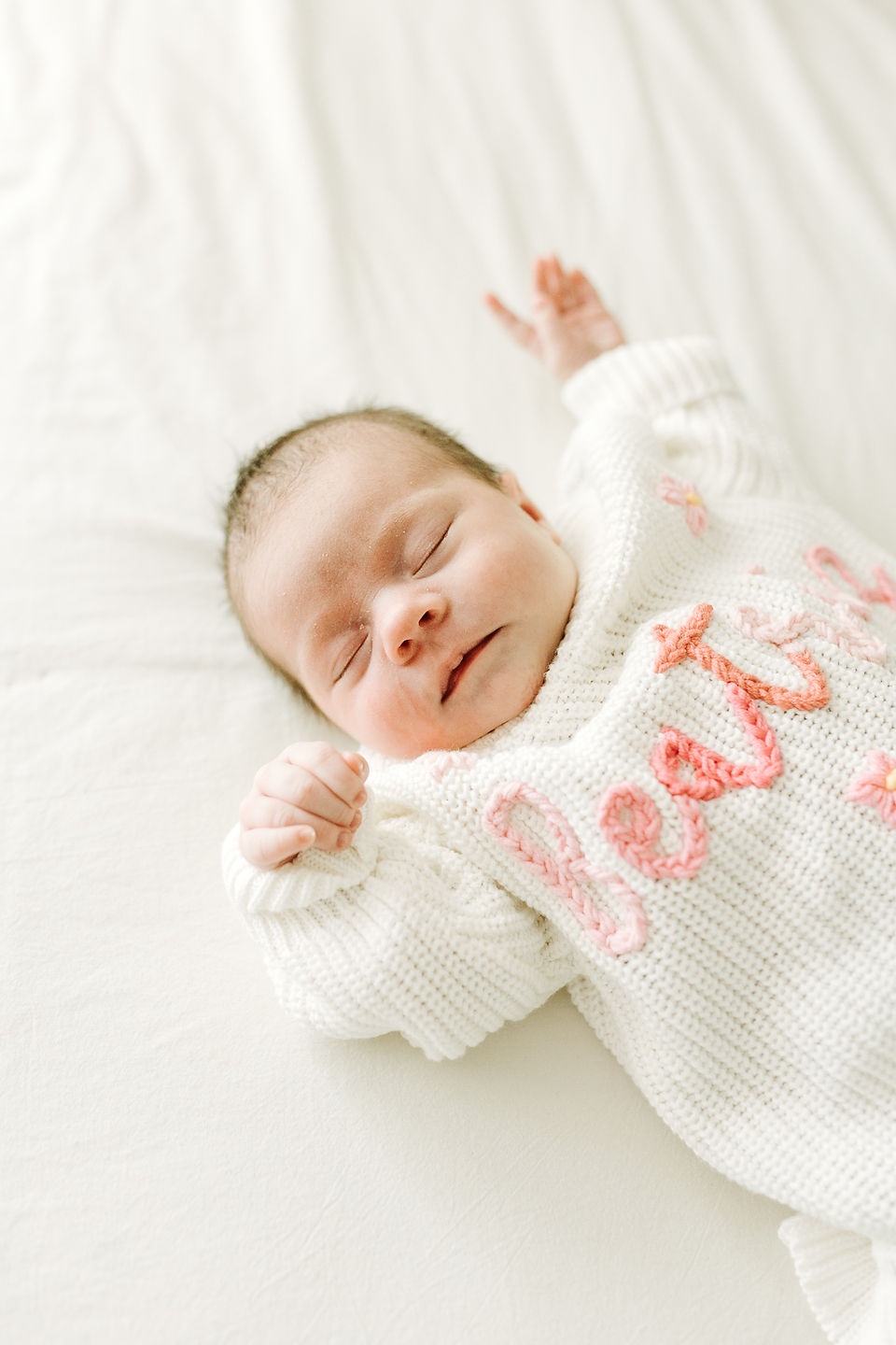 In-home newborn photography in Guelph, Ontario featuring a newborn baby wearing a white knit sweater with pink floral details