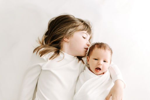 Newborn session in Guelph, Ontario capturing sister affectionately interacting with newborn baby in a bright, minimalist studio portrait