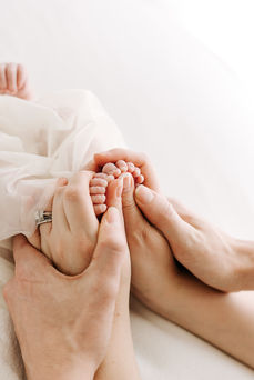 Newborn baby feet gently held by parents during a newborn session in Guelph, Ontario in soft cream fabric and natural studio lighting