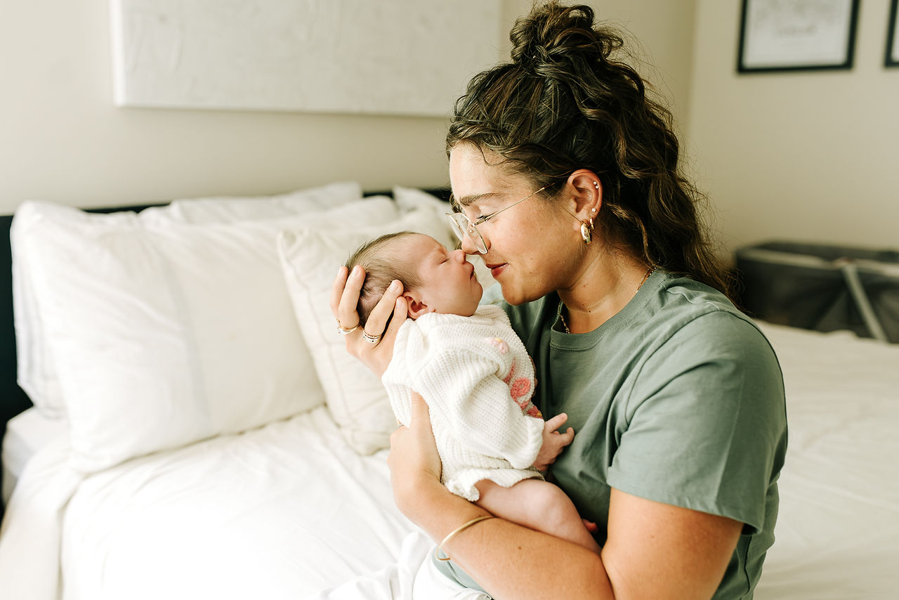 In-home newborn session in Guelph, Ontario featuring mom gently touching noses with her sleeping newborn baby on the bed