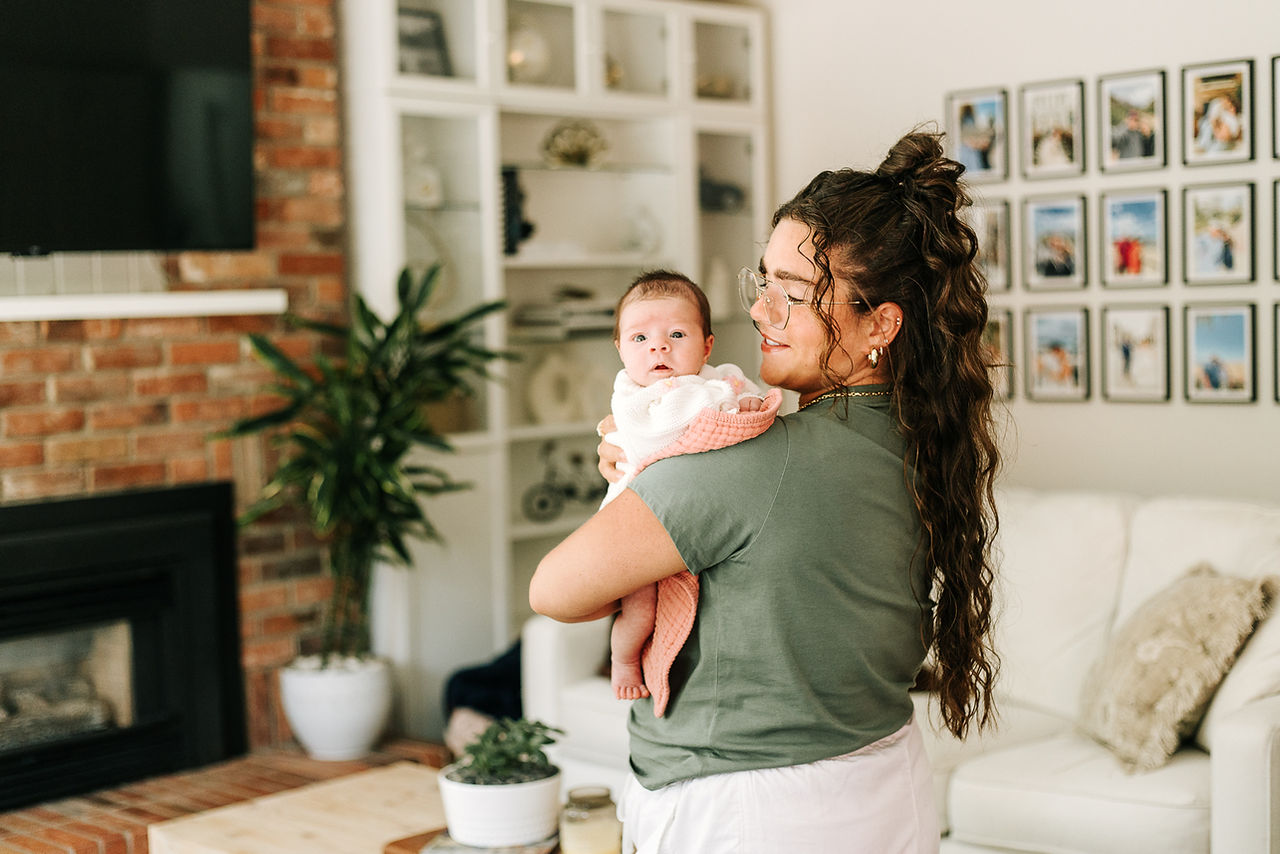 In-home newborn session in Guelph, Ontario featuring mother holding her newborn baby over her shoulder in a bright living room