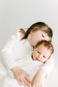 Newborn session in Guelph, Ontario capturing sister affectionately interacting with newborn baby in a bright, minimalist studio portrait