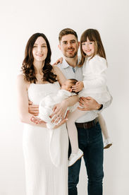 Newborn session in Guelph, Ontario featuring family of four with parents, newborn baby, and sibling posed against a clean white studio background