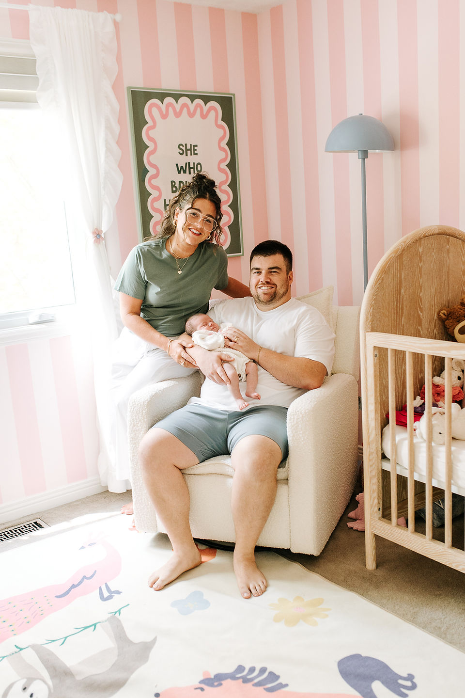 In-home newborn session in Guelph, Ontario featuring parents holding their newborn in a personalized nursery with hand-painted pink and white stripes