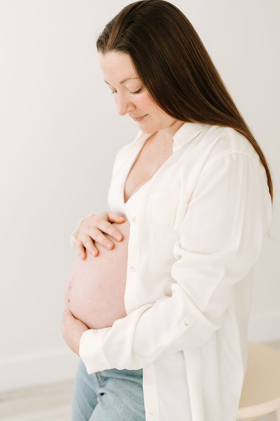 Mom-to-be in white bralette, white button-up shirt, and jeans during her maternity session at Elle Chic Photography Studio, Guelph