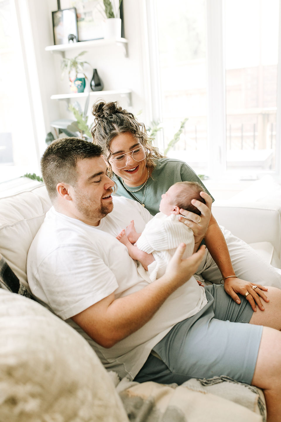 Newborn family photography in Guelph, Ontario capturing mom and dad cuddling their baby together on a light-colored couch