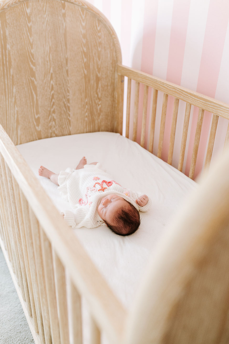 In-home newborn session in Guelph, Ontario featuring a sleeping baby in a white knit outfit resting in a wooden crib