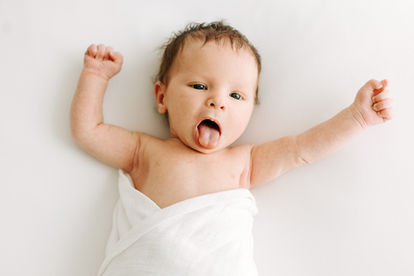 Newborn session in Guelph, Ontario featuring baby wrapped in white swaddle with arms outstretched in a bright, airy studio setup