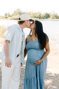 Maternity session in Guelph, Ontario featuring an expecting couple sharing a romantic kiss on the shoreline at Guelph Lake Conservation Area