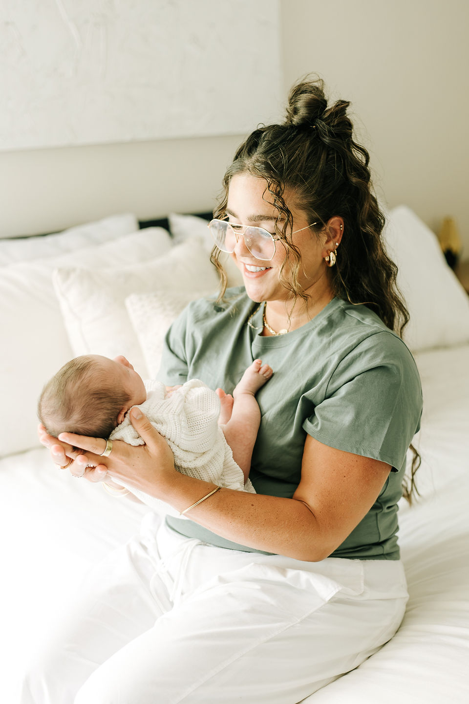 Cozy in-home newborn session in Guelph, Ontario featuring a mother holding her newborn baby girl against a neutral bedroom backdrop.