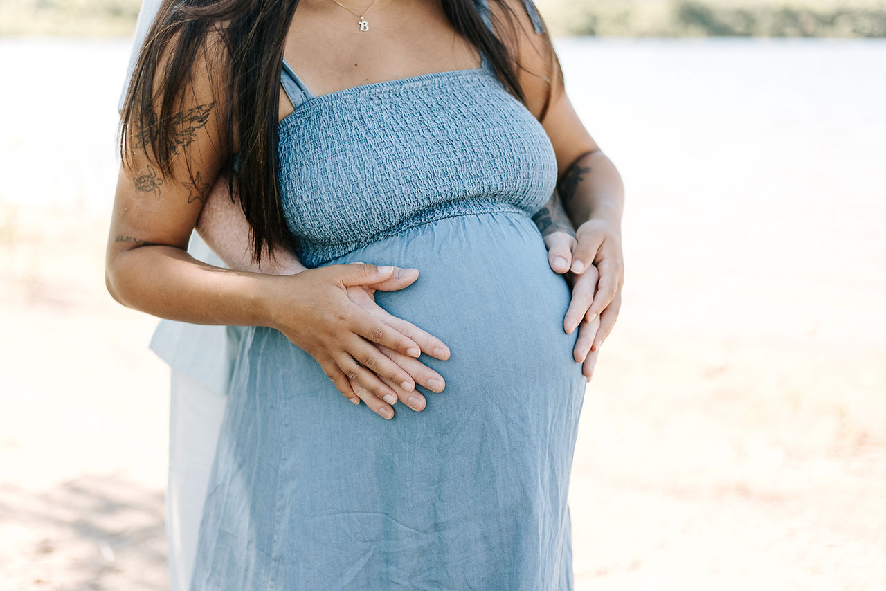 Expecting couple during a maternity session in Guelph, Ontario with hands resting on baby bump beside the lake