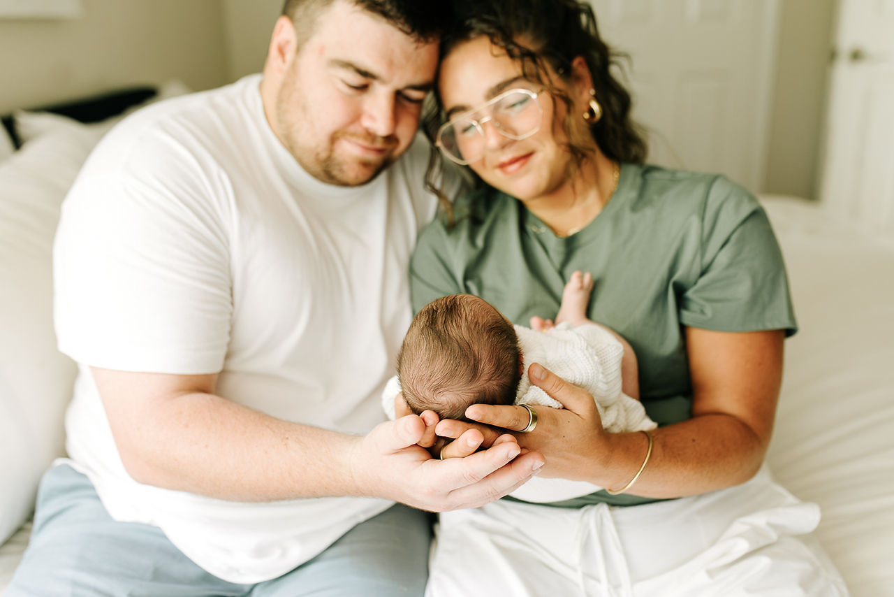 Natural newborn photography in Guelph, Ontario capturing parents holding their newborn baby in a relaxed home setting