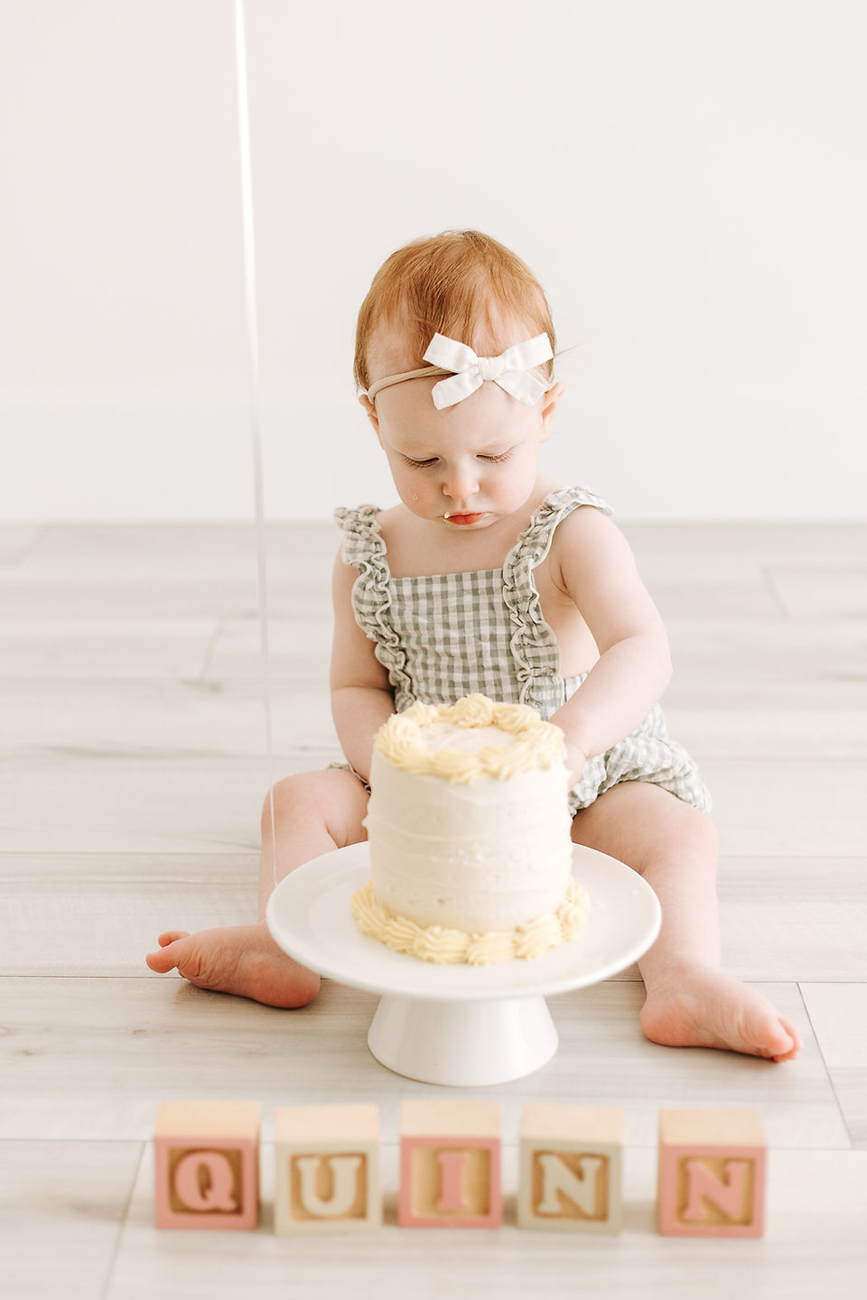 Cake smash session in Guelph, Ontario featuring baby girl smiling beside a simple white cake and neutral studio backdrop