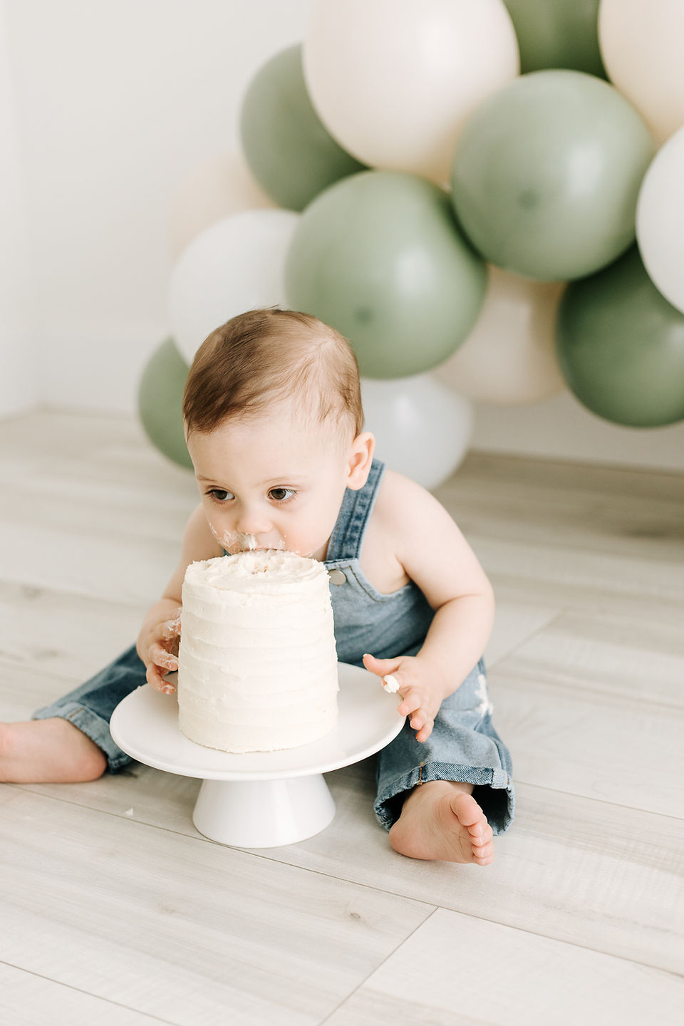 Baby wearing overalls sitting and eating cake during a From Maternity to Milestones session in Guelph, Ontario