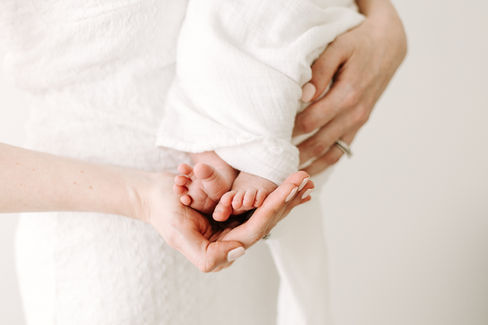 Close-up detail during newborn session in Guelph, Ontario showing parents gently holding newborn baby feet in a bright, minimal studio