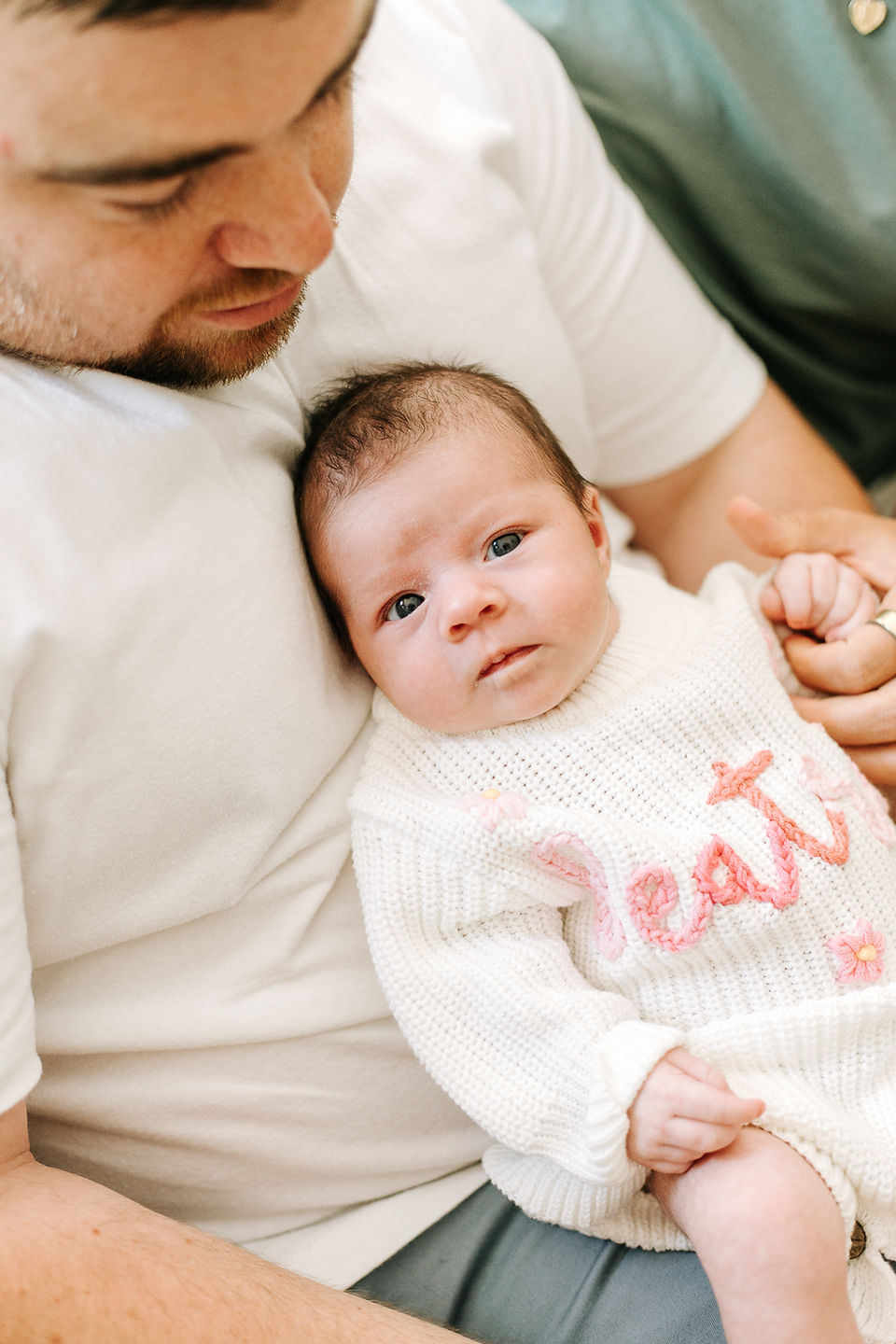 In-home newborn photography in Guelph, Ontario featuring a newborn baby wearing a white knit sweater with pink floral details