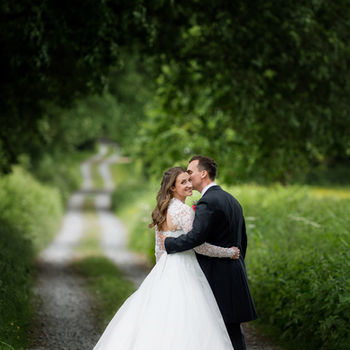 A bride in white dress and groom in black suit. She looks back at the camera during portraits on a country lane