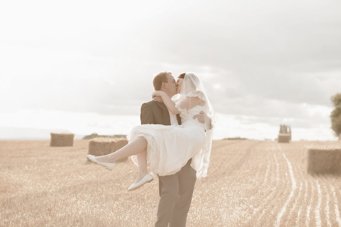 Bride and groom sharing a kiss as the groom lifts the bride in a harvested field during relaxed wedding portraits at Lyde Arundel