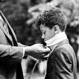 On the morning of a wedding a young boy has his tie put on by his father