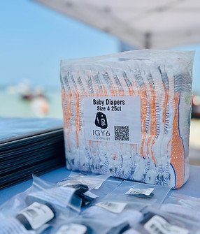 A package of baby diapers branded by IGY6 Company on display at an outdoor event, with a clear blue sky in the background.