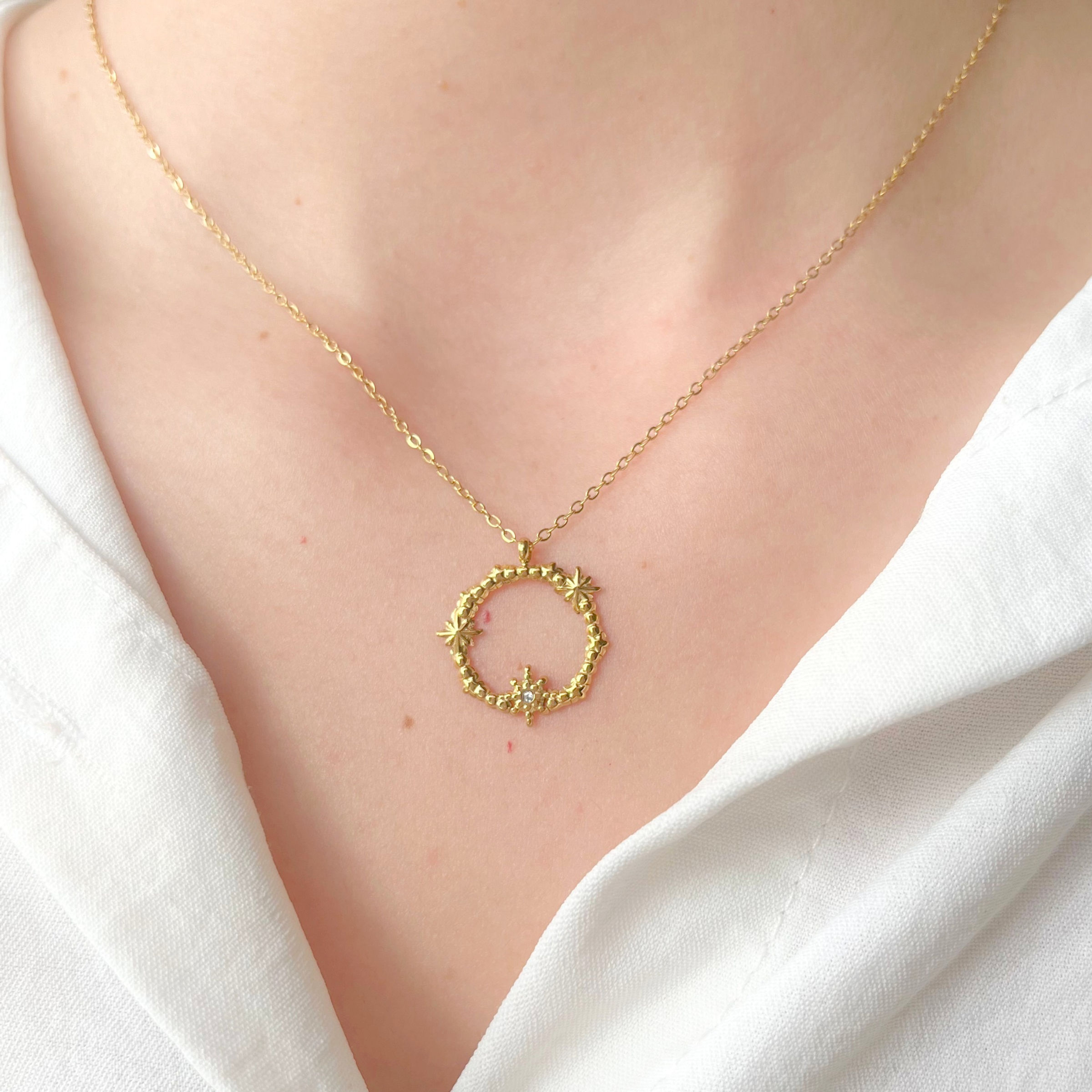 Collier en acier inoxydable doré pendentif cercle orné de trois petites étoiles, une avec un strass.
