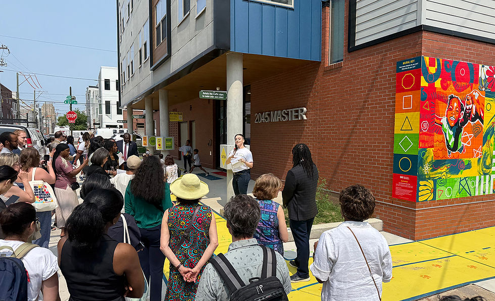 A large group stands at the corner of a building while an architect speaks to them.