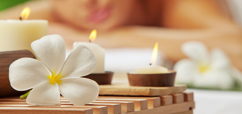 Relaxing spa scene with candles and white plumeria flower symbolizing tranquility and self-care at Presence Wellness Center and Spa in Auburn, CA.