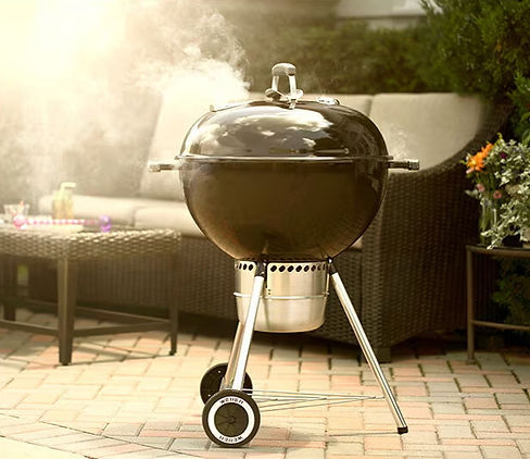 Close-up of a Weber Original Kettle charcoal grill with lid open, showing glowing embers.