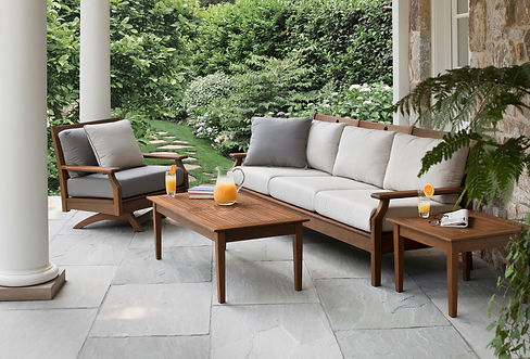 Jensen Outdoor Opal Collection Ipe wood sofa and coffee table with grey cushions, showcased in a beautiful garden setting with orange juice pitcher.