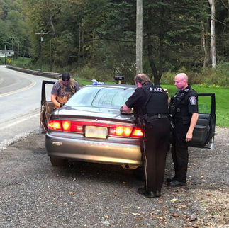 Two officers conducting a traffic stop on a gray sedan roadside.