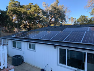 Solar panels on a house rooftop under a clear blue sky. Trees in the background and a white fence in the foreground.