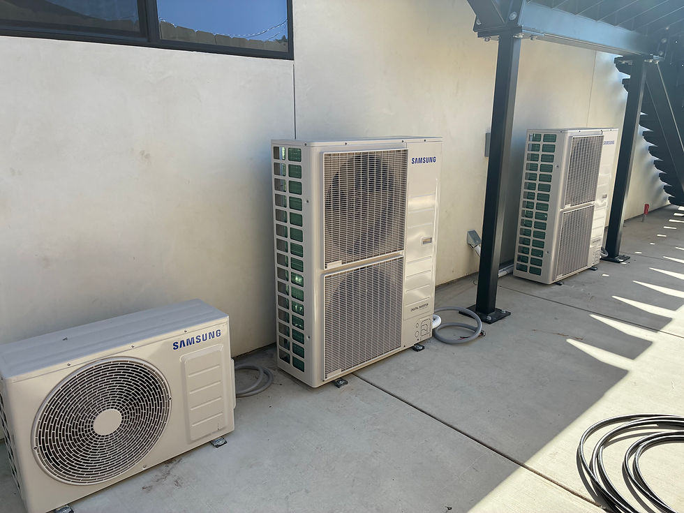 Three Samsung air conditioning units in a concrete outdoor setting, under a staircase. Natural sunlight casts shadows on the ground.